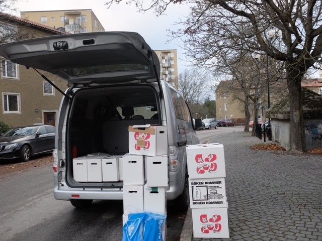 Lådor med böcker vid en bil med öppen baklucka.