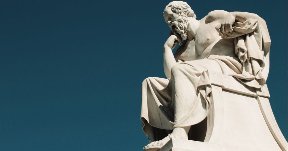 Bild på en staty mot blå bakgrund, sittande man lutar hakan mot armen.