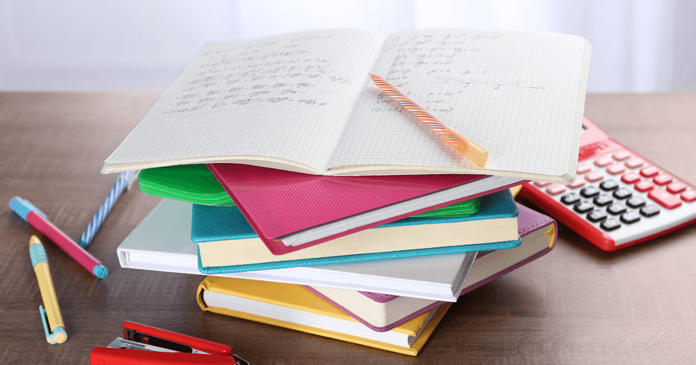 Bild på trave böcker, miniräknare och pennor på ett bord. 