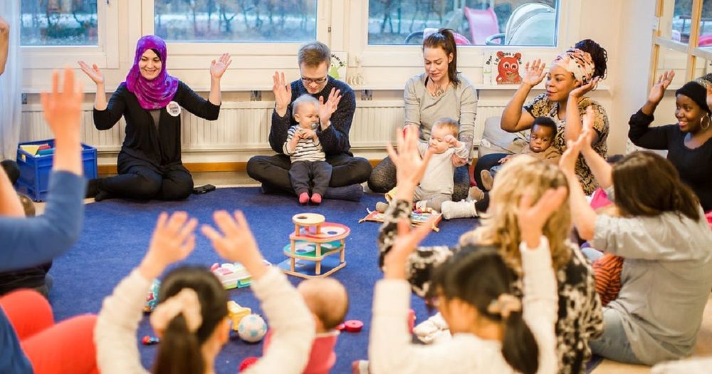 Vuxna och bebisar sitter i en ring med uppsträckta armar.