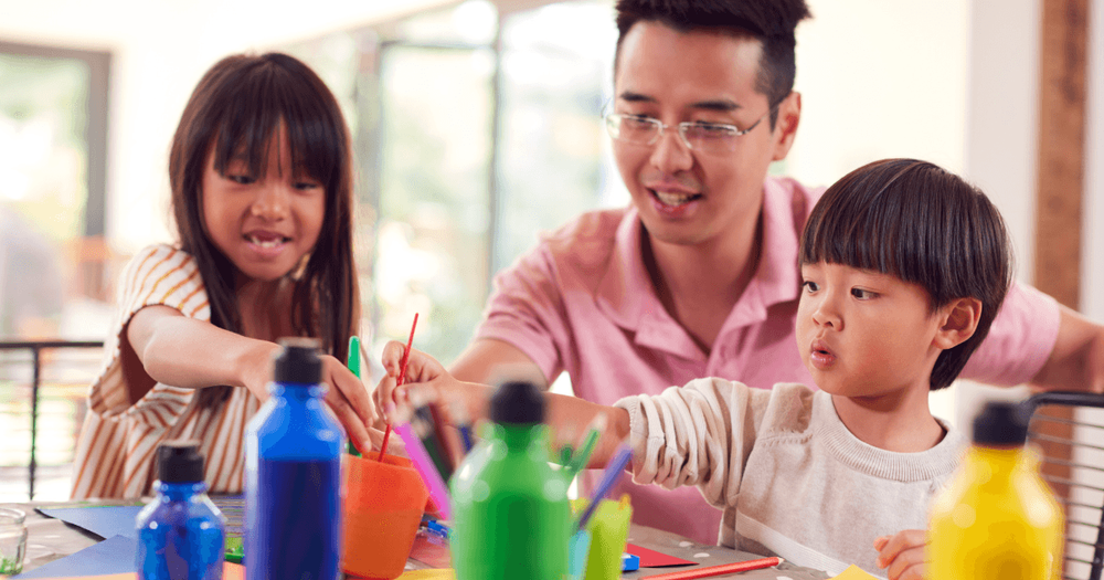Två barn och en pappa sitter vid ett bord och målar. 