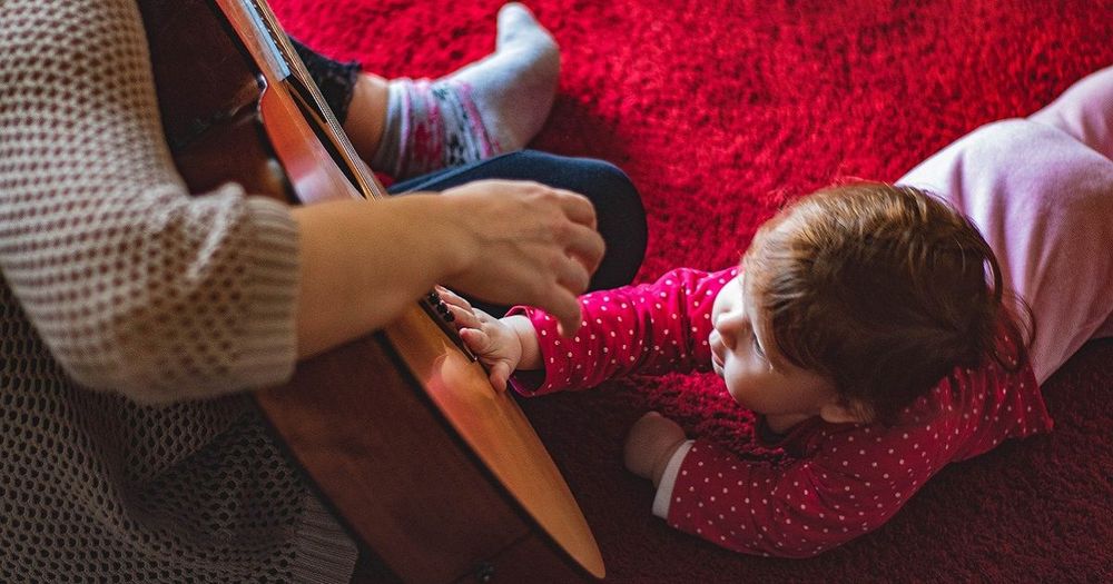 En bebis på en röd matta klappar på en gitarr.