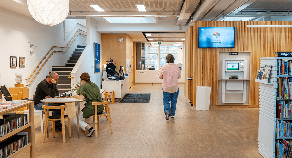 Interiör från Kungsholmens bibliotek Internationella biblioteket, med två personer som spelar schack och en person som går bort från kameran.