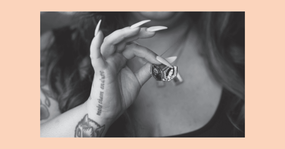 Stillbild från filmen These Patrified Paths på en kvinnohand som håller upp en berlock. 