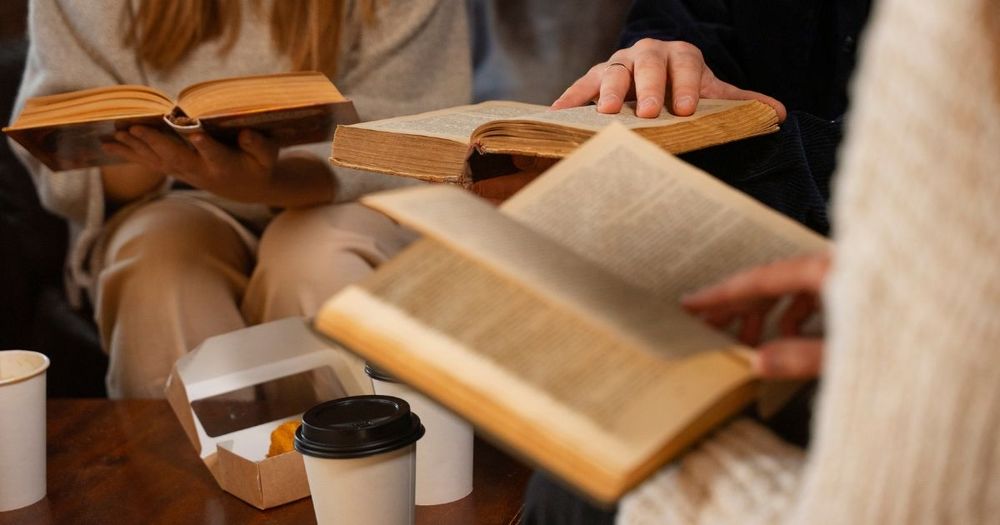 Tre personer med en varsin bok i handen och kaffekoppar framför sig